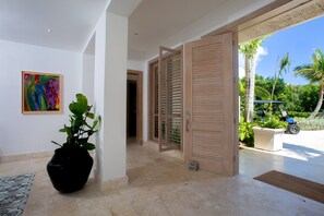 A hallway with a potted plant, a colorful abstract painting, and a wooden door leading outside.