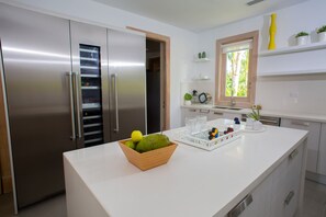 A modern kitchen with stainless steel appliances, a white countertop, and a window with a view of greenery.