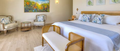 A bedroom with a large bed, two chairs, a bench, a painting, and wall-mounted lights.