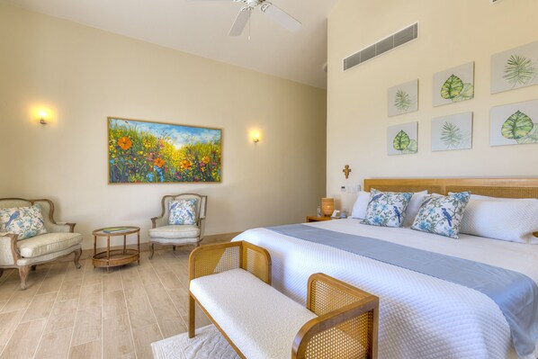 A bedroom with a large bed, two chairs, a bench, a painting, and wall-mounted lights. - Villa Calista Elegant Holiday Villa (Adeje)