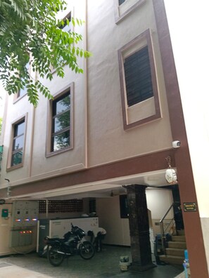 Un edificio con acceso a garaje, una motocicleta estacionada en su interior y una escalera que conduce a un nivel superior.