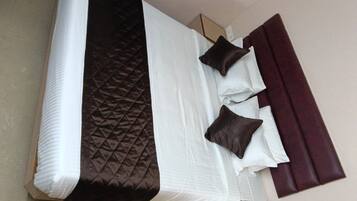 Un lit simple avec une tête de lit matelassée, deux oreillers et un rideau de couleur foncée.