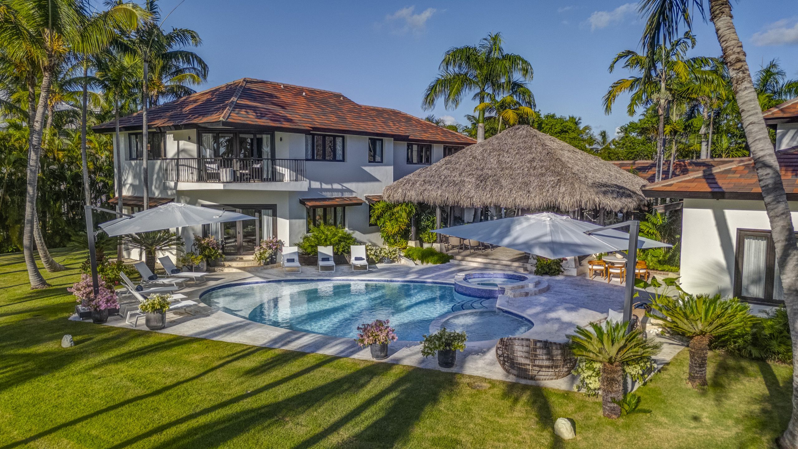 A pool area with lounge chairs, umbrellas, and a thatched-roof structure.