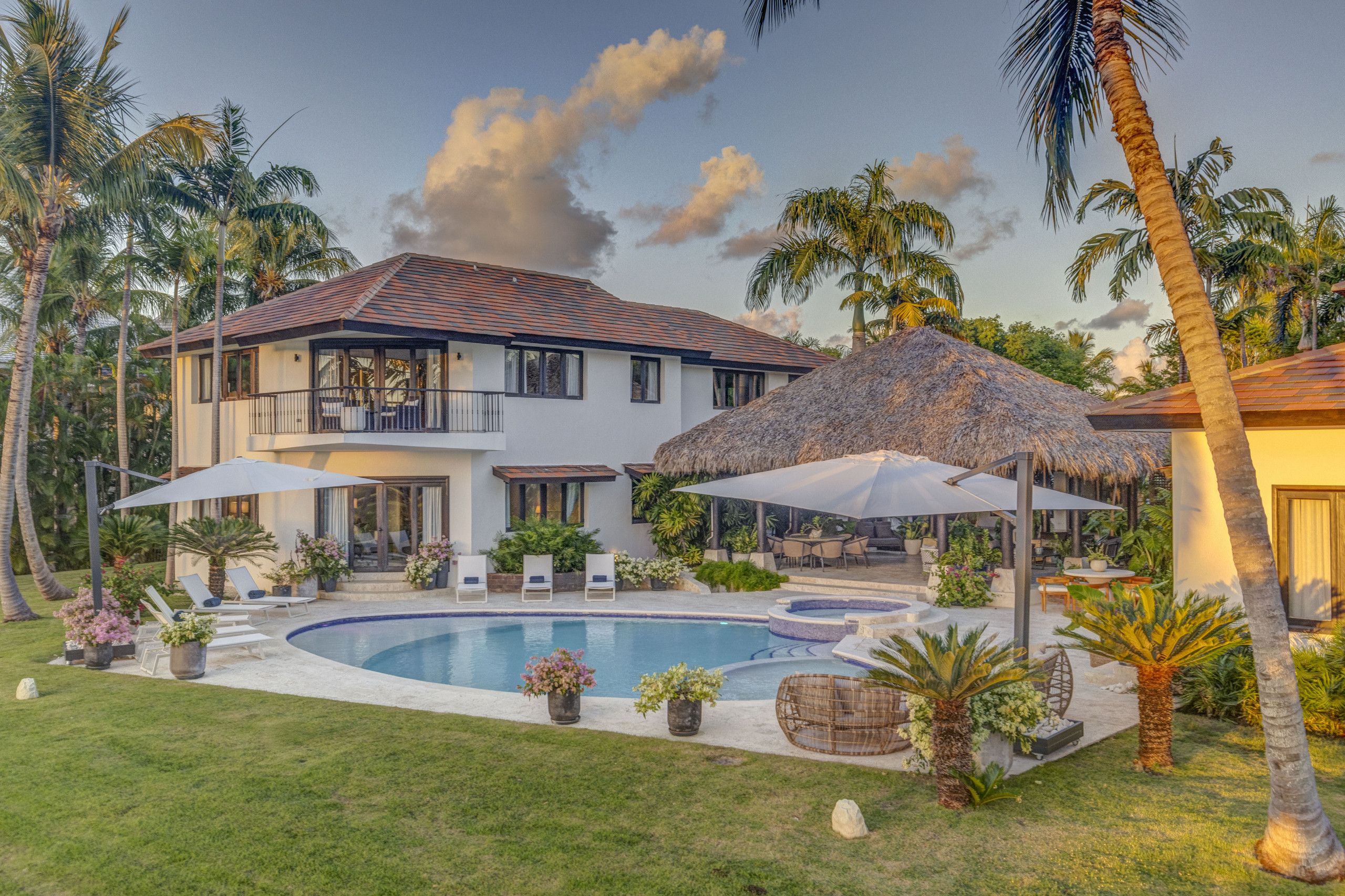 A two-story house with a swimming pool, outdoor seating, and palm trees.