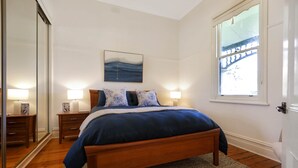 Ein Schlafzimmer mit einem hölzernen Bett, zwei Nachttischen, einem Schreibtisch und einem an der Wand hängenden Gemälde.
