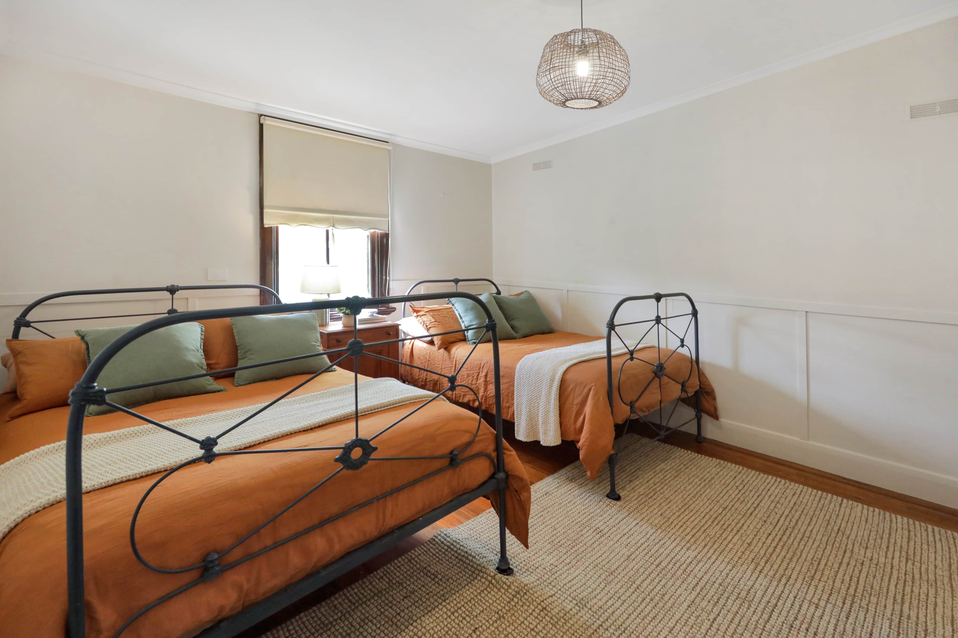 Quarto com duas camas, janela com cortina, mesa de cabeceira e luminária suspensa.