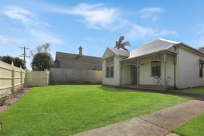 A residential property with a well-maintained lawn, a wooden fence, and a two-story house with a porch. - Fig Tree Cottage on Koroit | Central Warrnambool (Warrnambool)