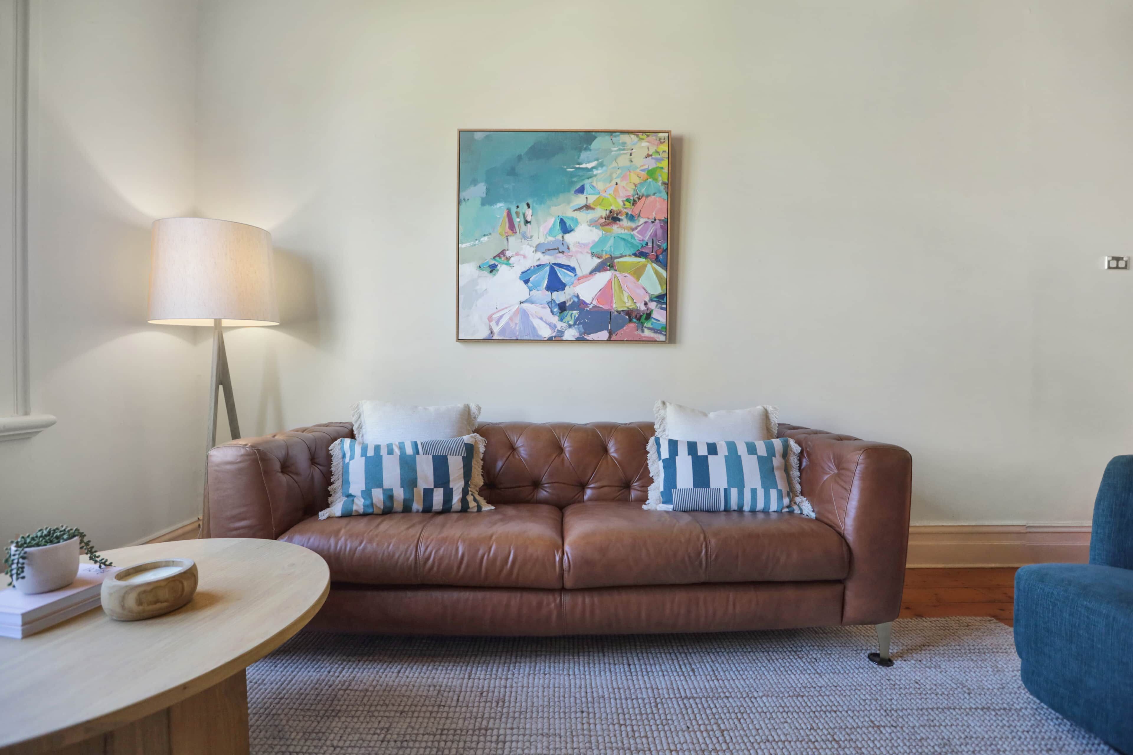 A brown leather sofa with striped pillows, a round wooden coffee table, and a floor lamp.