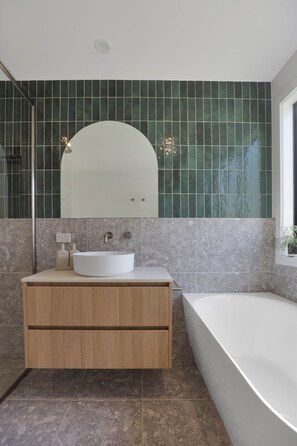 A bathroom with a freestanding bathtub, a vanity with a sink, and a mirror above the vanity. - Fig Tree Cottage on Koroit | Central Warrnambool (Warrnambool)