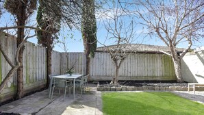 Ein Garten mit Terrassentisch und -stühlen, einer kleinen Rasenfläche und einem Holzzaun.