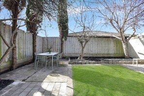 A backyard with a patio table and chairs, a small lawn, and a wooden fence. - Fig Tree Cottage on Koroit | Central Warrnambool (Warrnambool)