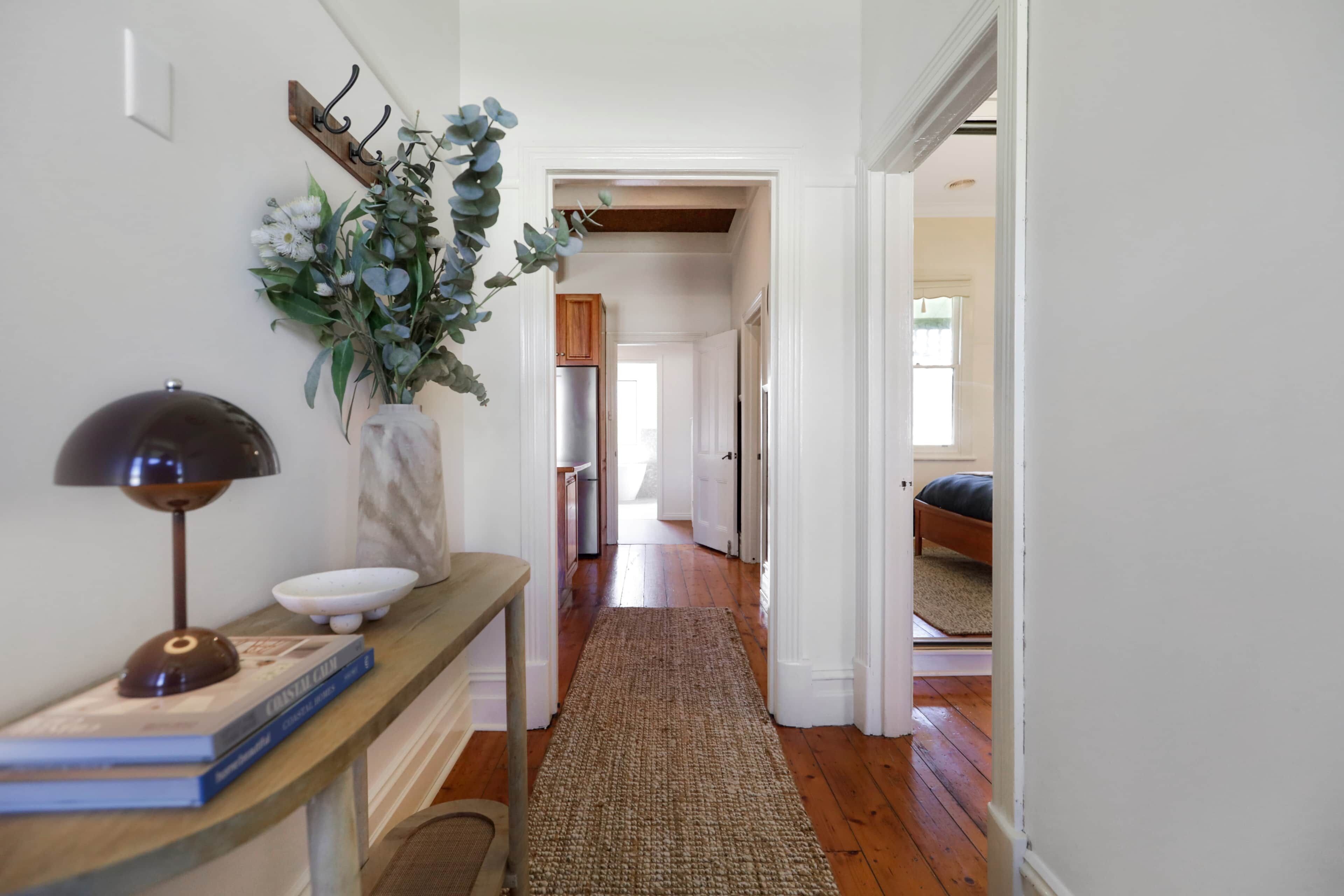 A hallway with a wooden bench, a vase with flowers, and a lamp.