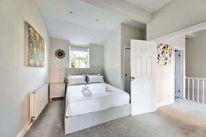 A bedroom with a bed, a nightstand, a radiator, a window with blinds, and a door leading to another room. - Elegant St Johns Wood Mews-King Bed & Workspace (London)