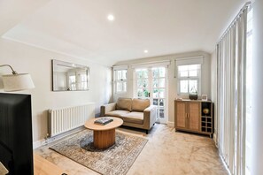 A modern living room with a sofa, a coffee table, a cabinet, and a radiator. - Elegant St Johns Wood Mews-King Bed & Workspace (London)