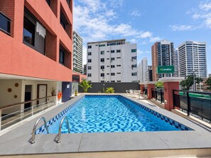 An outdoor swimming pool with a tiled floor, surrounded by a building with a red facade and a sign for 'Localiza'. - Flat Moderno, 2 Quartos Dentro de Hotel Famoso (Fortaleza)