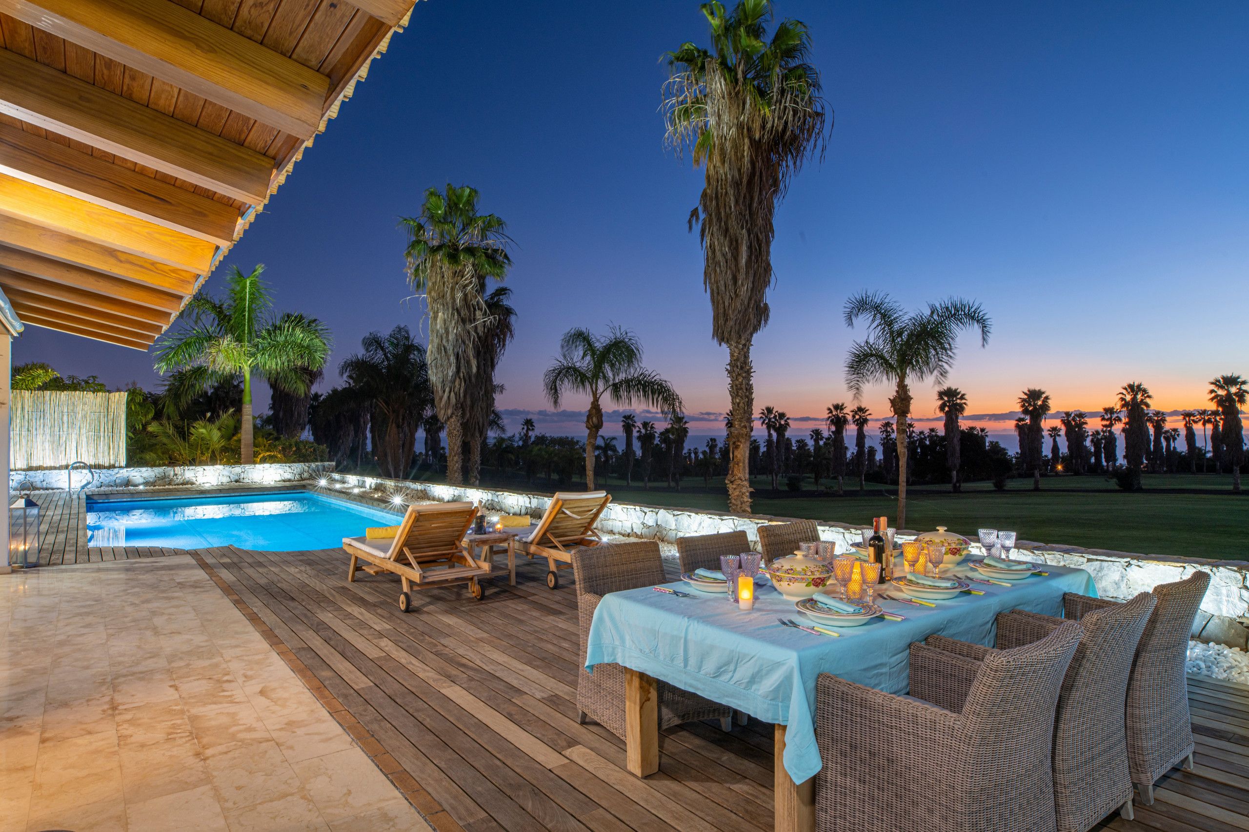 Un espace extérieur aménagé pour les repas, avec une piscine, une terrasse en bois et des palmiers.