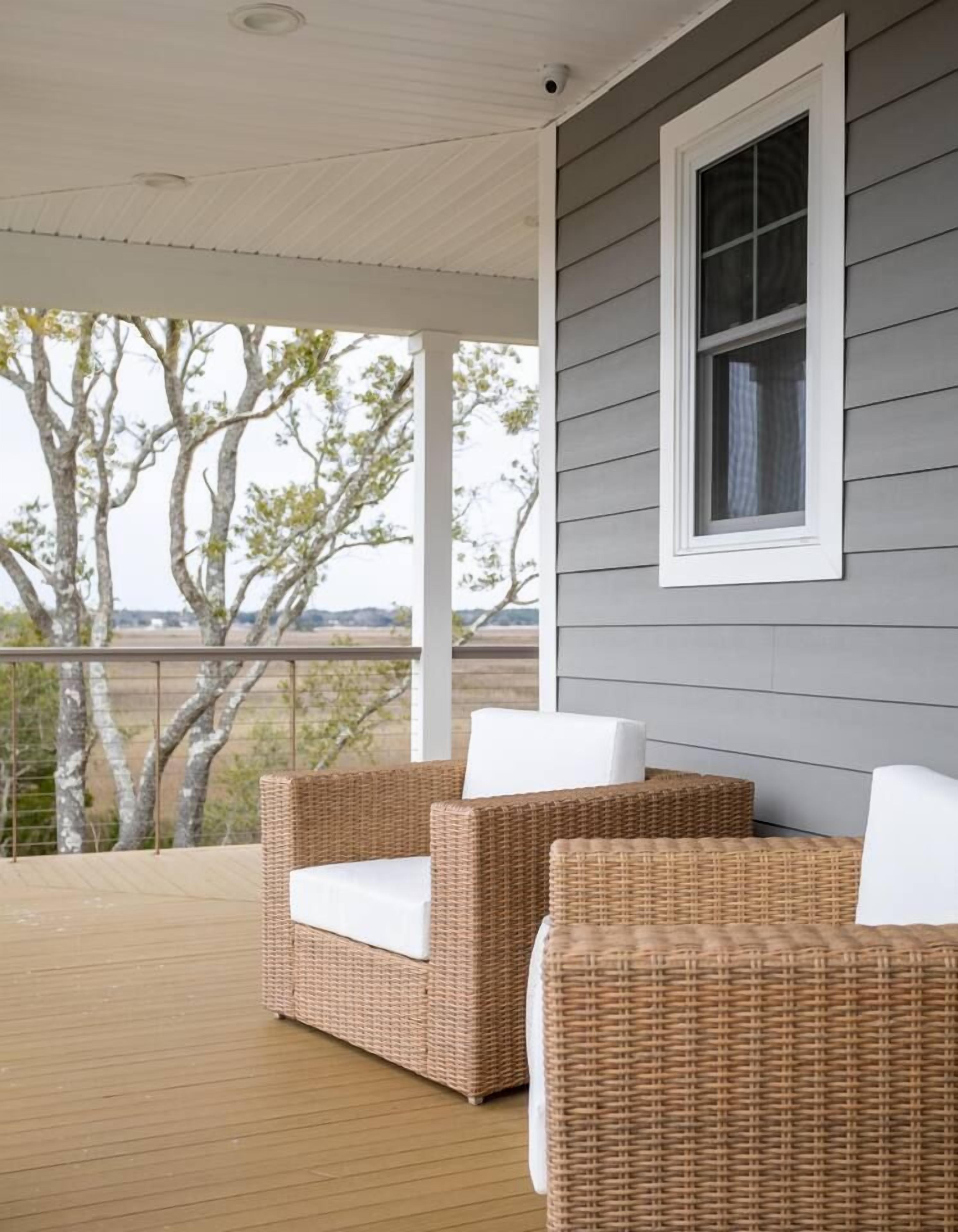 A covered porch with wicker furniture and a view of trees.