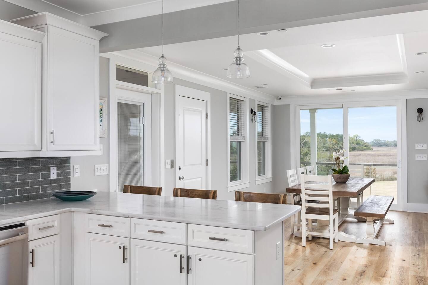 A modern kitchen with white cabinetry, a marble countertop, and a dining area with a wooden table and chairs.