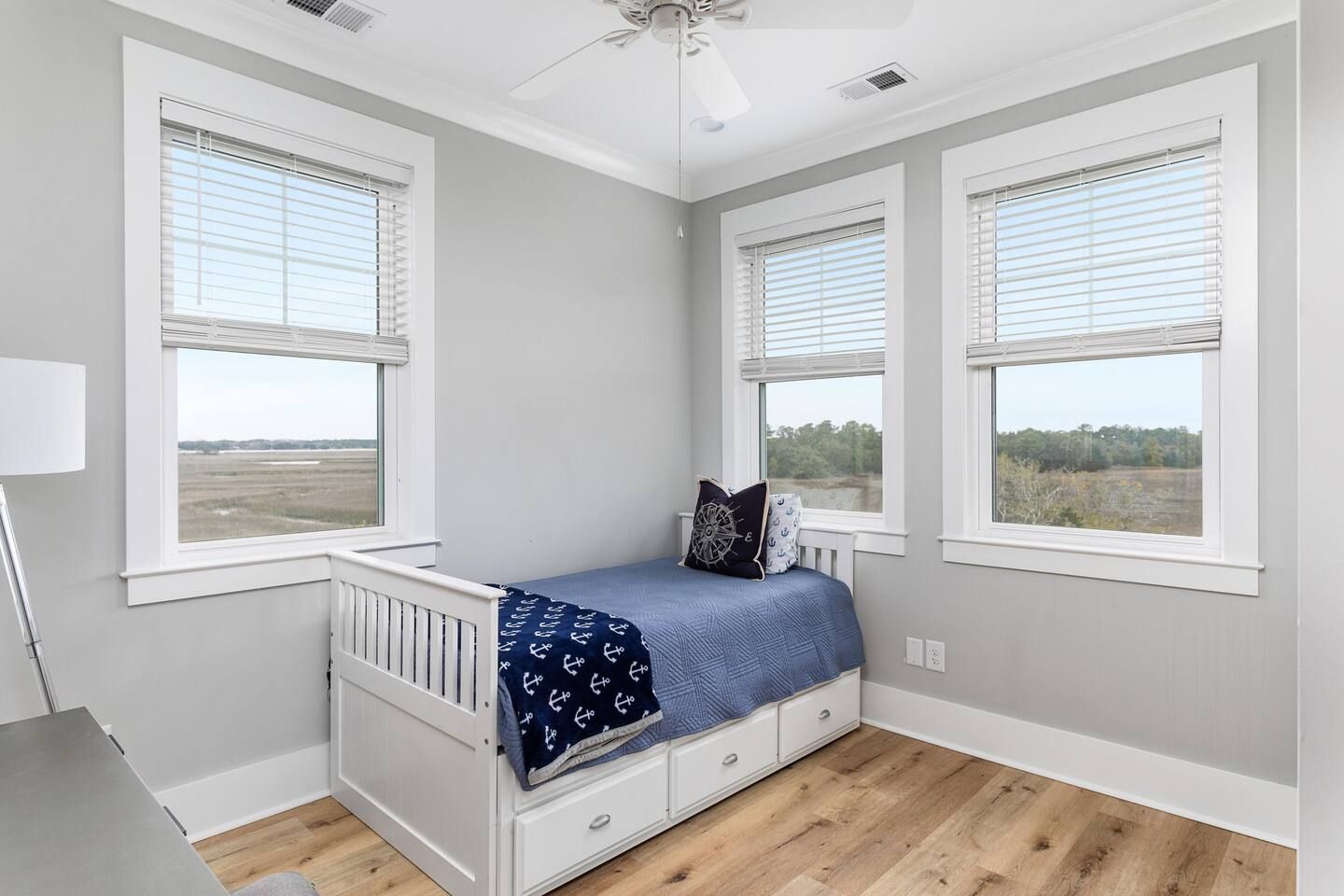 A room with a single bed, two windows, and a ceiling fan.