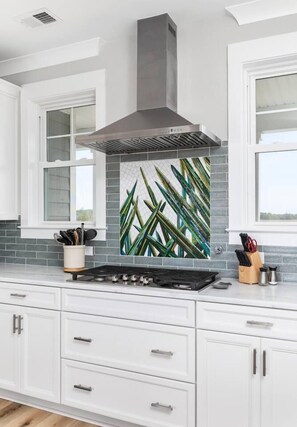 Cozinha com armários brancos, exaustor de aço inoxidável e painel decorativo com padrão de folhas.