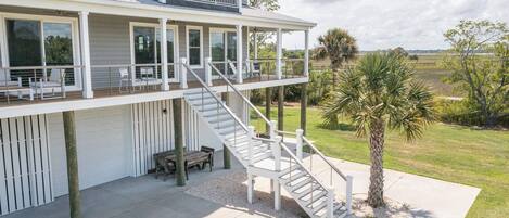 A two-story house with a covered patio, outdoor seating, and a staircase leading to a balcony.
