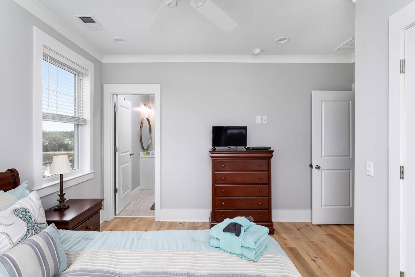 A bedroom with a bed, a dresser, a television, and a window with blinds.