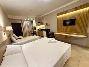 A hotel room with a bed, a desk, a chair, a TV, and a kitchenette.