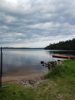 A calm lake with a dock, surrounded by grassy areas and trees.