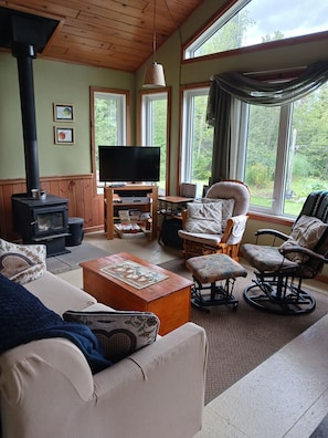 A cozy living room with a fireplace, comfortable seating, a television, and large windows offering a view of the outdoors. - Remote Lakeside Cabin | Fall Fishing, Hunting & Northern Ontario Views (Flanders)