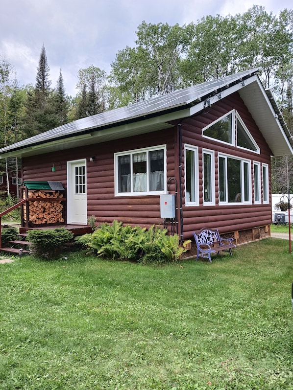 A log cabin with a porch, a bench, and a stack of firewood. - Remote Lakeside Cabin | Fall Fishing, Hunting & Northern Ontario Views (Flanders)