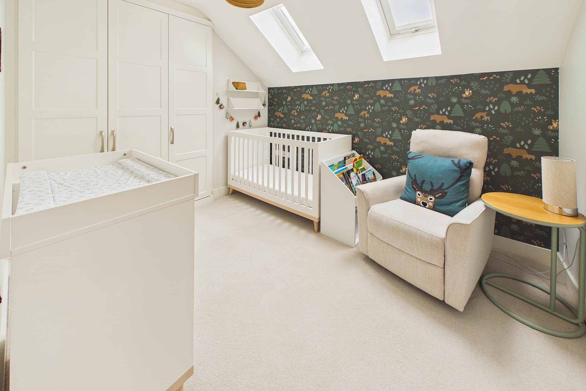 A baby room with a crib, a changing table, a high chair, and a wall with a forest animal print.