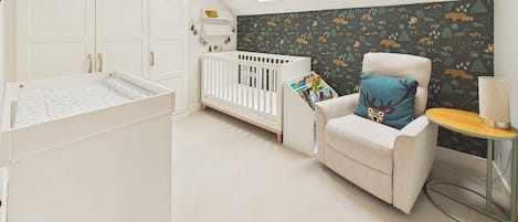 Una habitación infantil con cuna, un cambiador, una trona e impresión de animales del bosque en la pared.