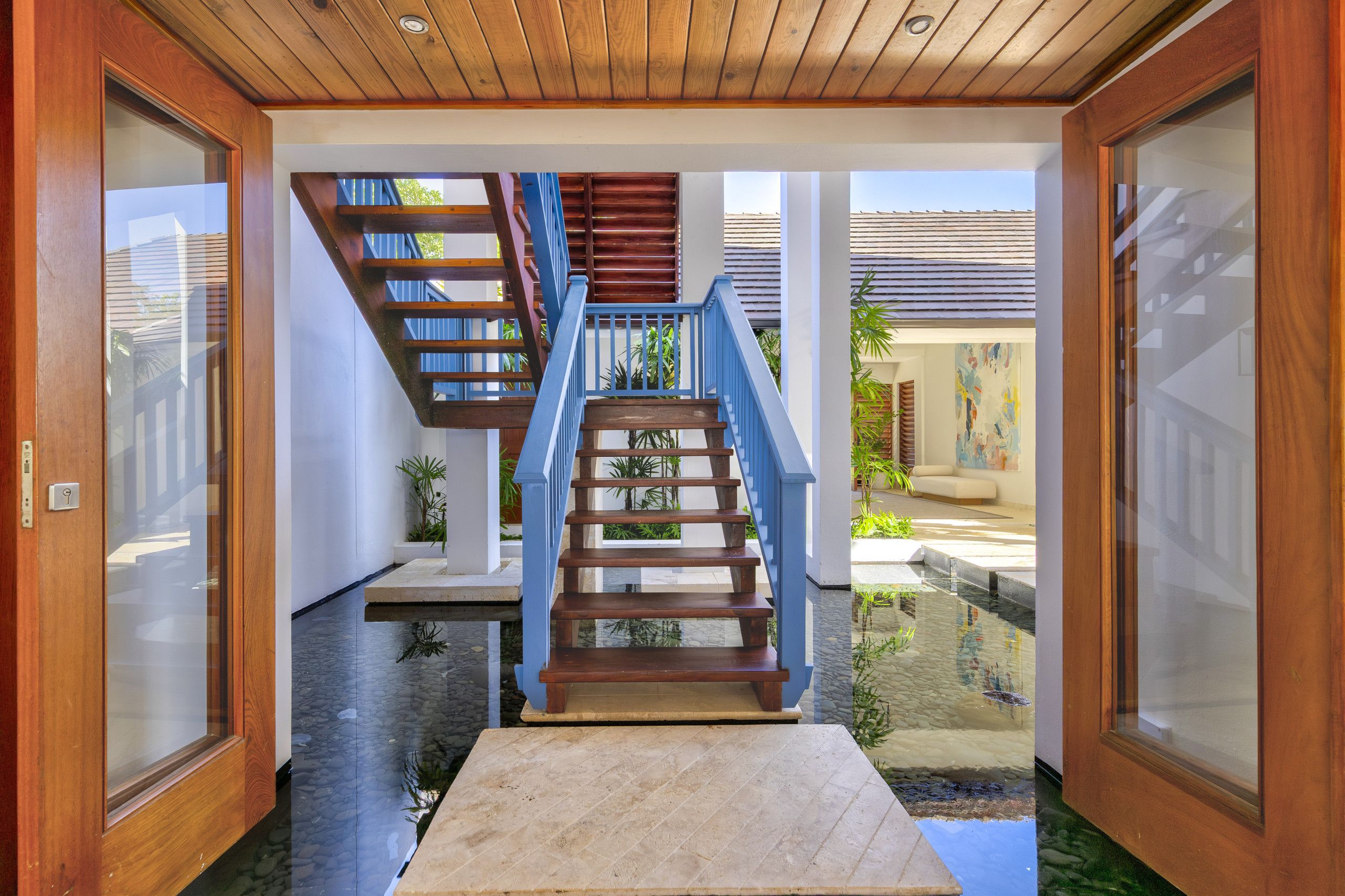 A wooden staircase with blue railings leading to a landing, surrounded by glass doors and a tiled floor.