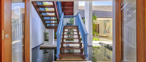 A wooden staircase with blue railings leading to a landing, surrounded by glass doors and a tiled floor.