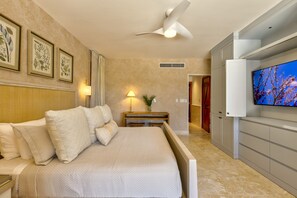 A hotel room with a bed, a TV, a ceiling fan, and framed botanical artwork on the wall.