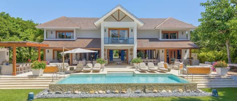 Una casa de dos pisos con piscina, mobiliario exterior y jardín.