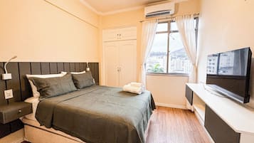 A bedroom with a bed, bedside table, TV, and a window with curtains.