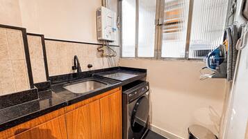 A compact kitchen with a sink, stove, and oven, wooden cabinets, and a window with blinds.