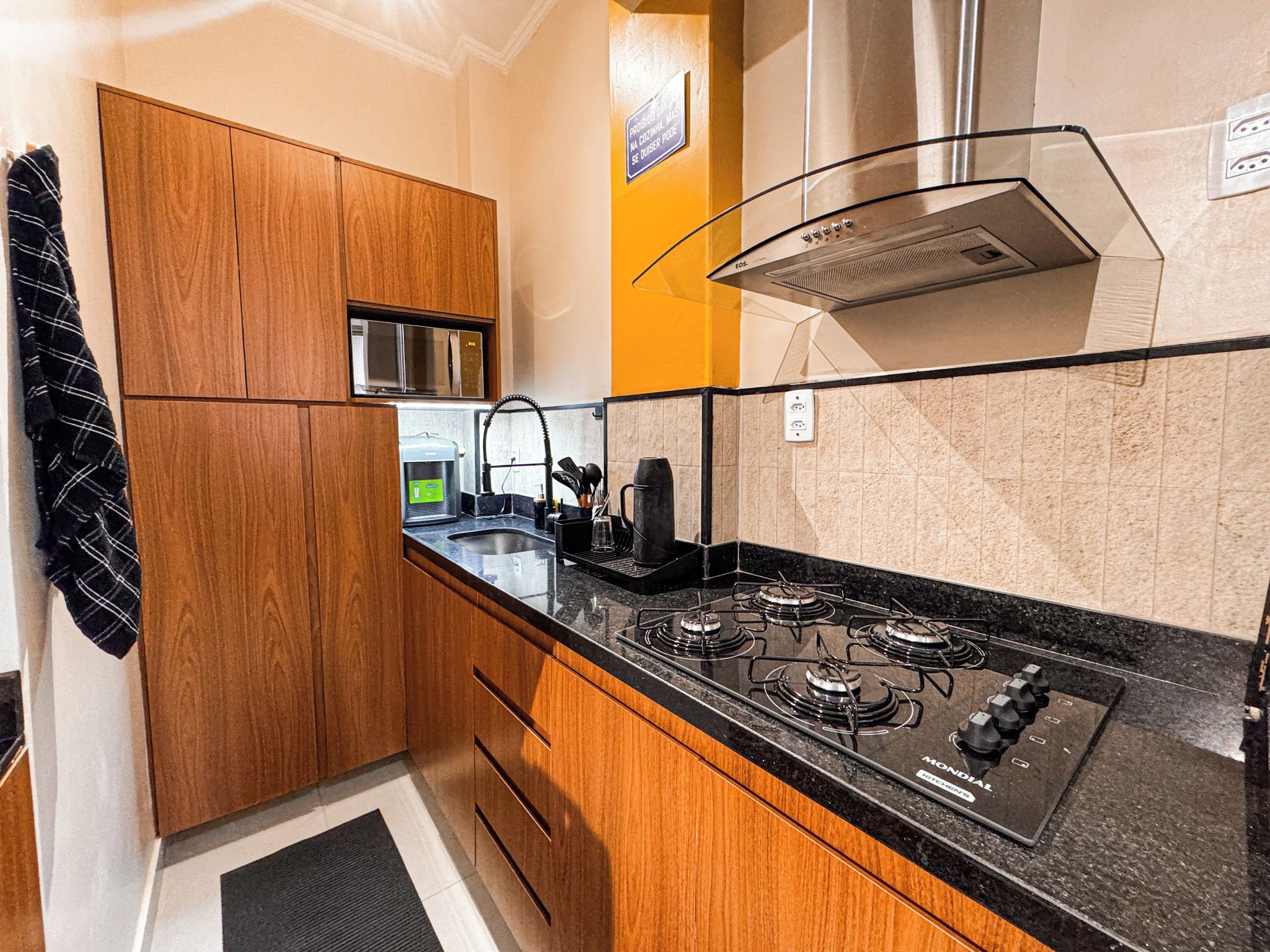 A compact kitchen with wooden cabinets, a gas stove, a stainless steel range hood, and a water dispenser.
