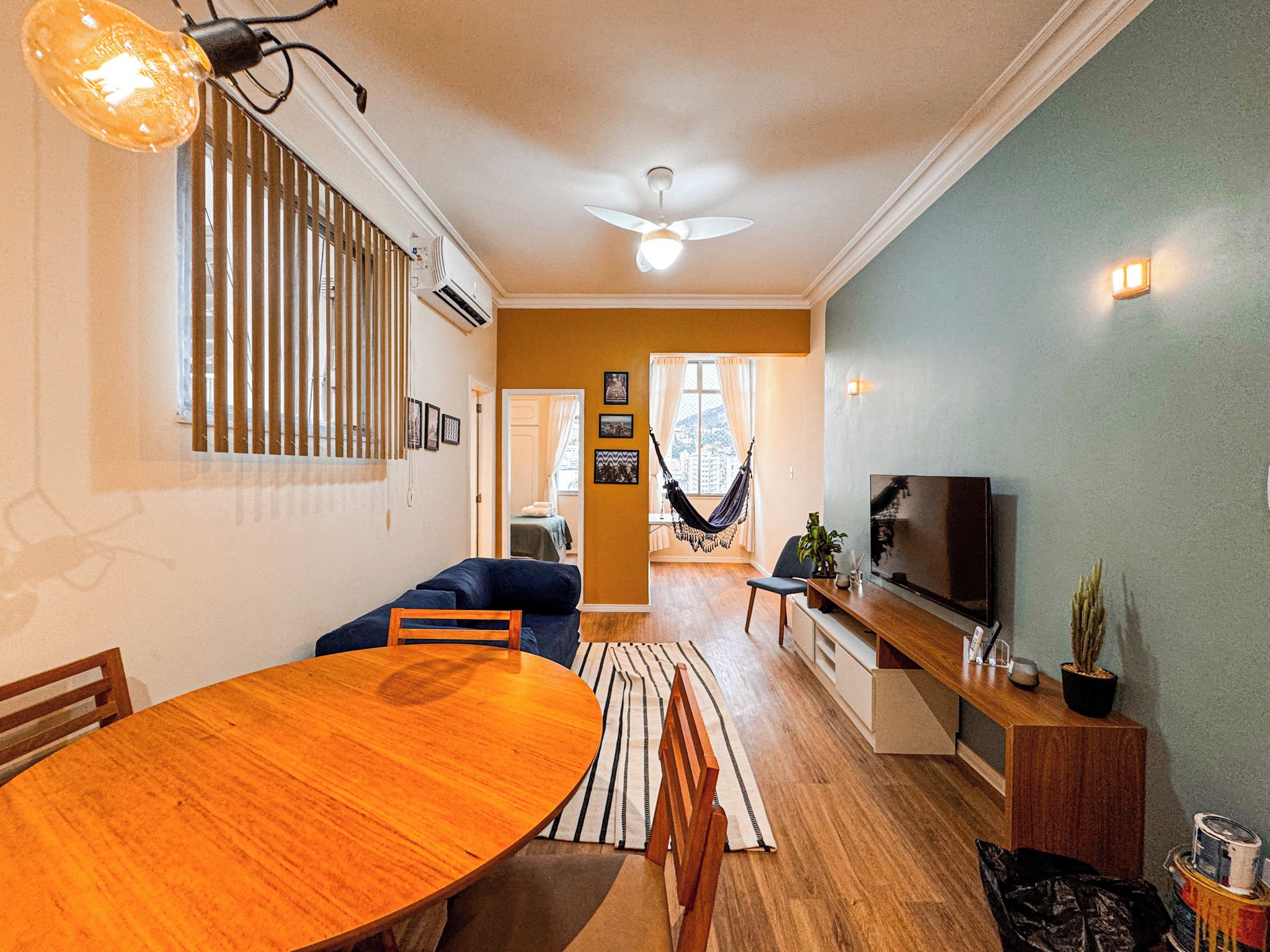 A modern living room with a dining table, sofa, TV, and a hammock.