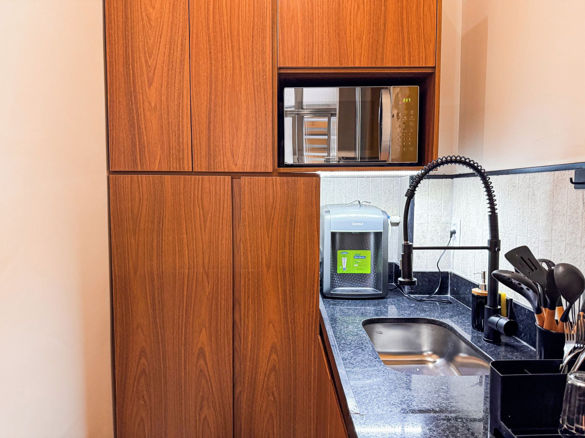 A compact kitchen with wooden cabinets, a stainless steel sink, a coffee maker, and a set of kitchen utensils.