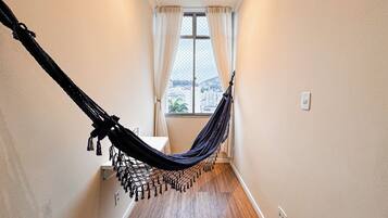 A hallway with a hammock, a window with curtains, and a view of buildings outside.