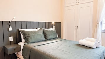 Ein ordentlich bezogenes Bett mit dunkelgrüner Bettdecke und Kissen, ein Nachttisch mit Lampe und ein Schrank mit Spiegel.