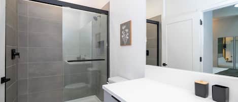 A modern bathroom with a glass shower enclosure, a white toilet, and a white vanity with a mirror.