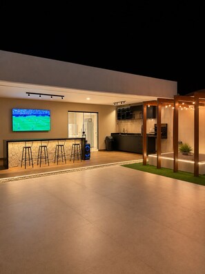 A modern outdoor bar area with a flat-screen TV, bar stools, and a kitchen area with a grill.