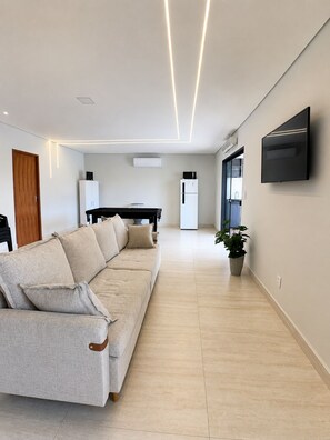 A modern living room with a sofa, a flat-screen TV mounted on the wall, and a potted plant.
