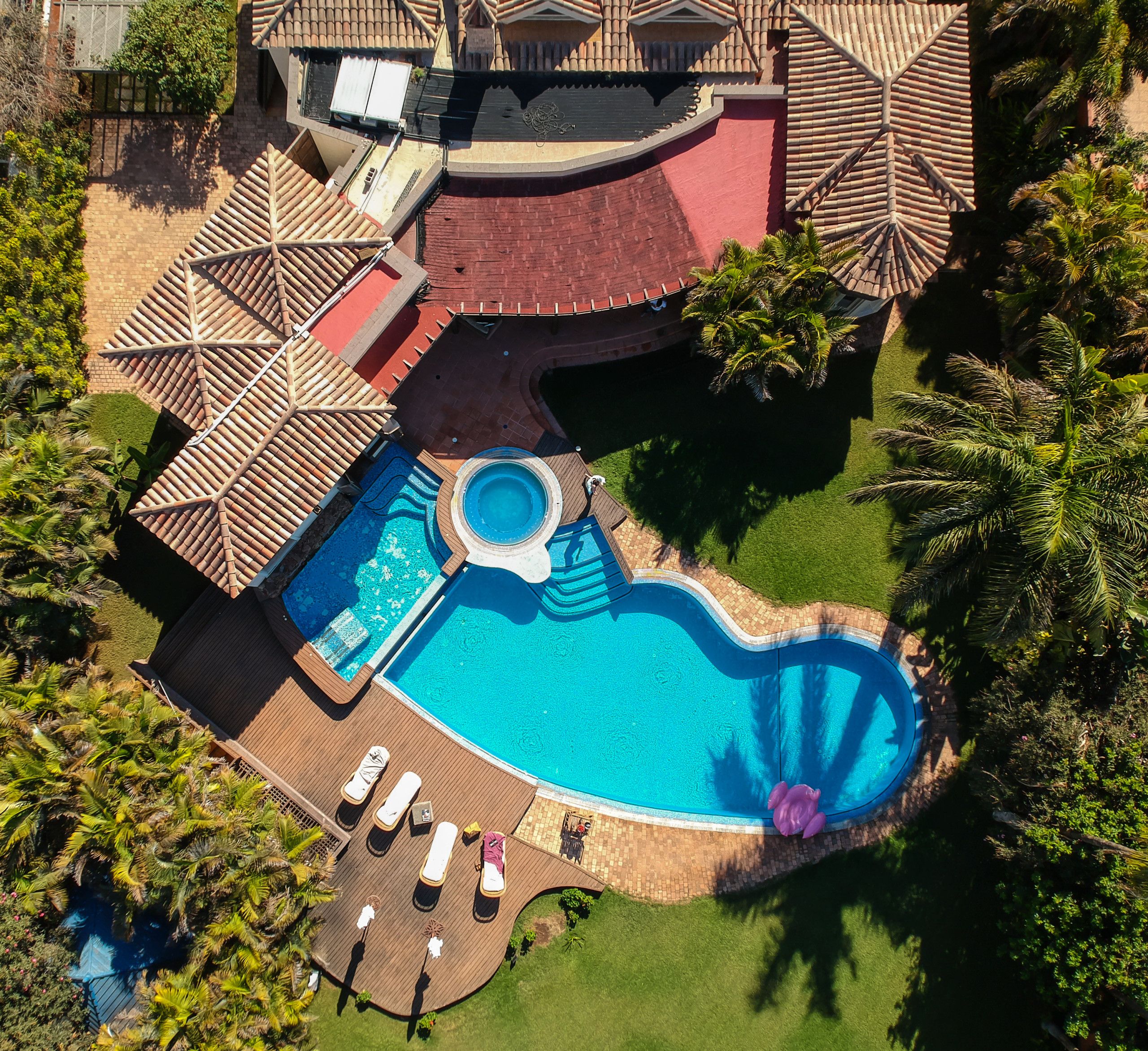 Vue aérienne d’un complexe hôtelier avec une piscine, des chaises longues et des palmiers.