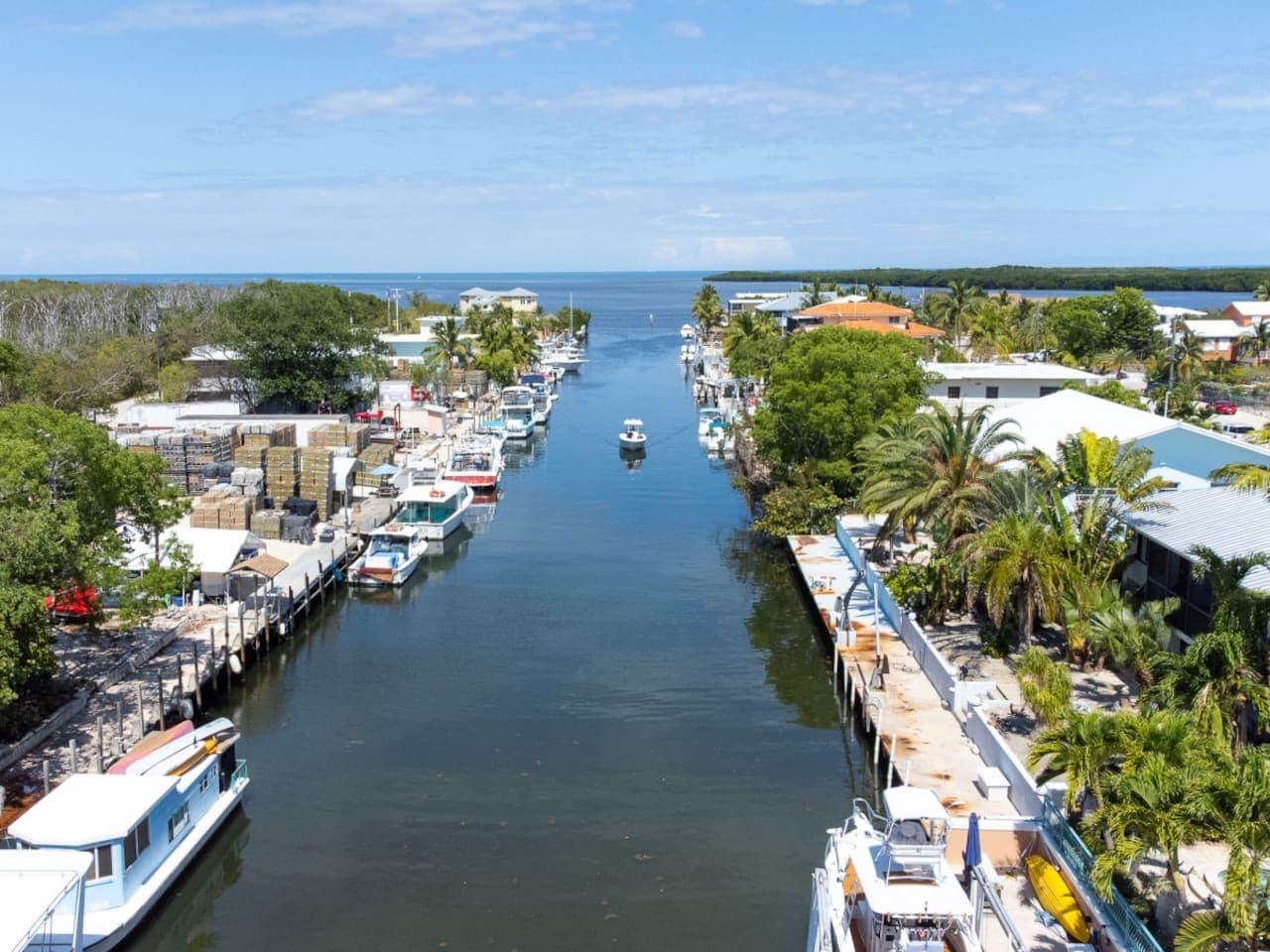 A marina with boats docked along a narrow waterway, surrounded by buildings and greenery.