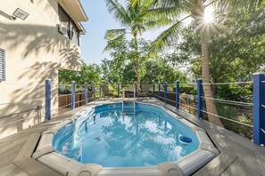 A swimming pool with a wooden deck, surrounded by a blue fence, and palm trees in the background.