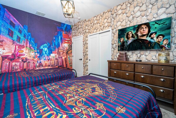 Ein Schlafzimmer mit einer Stadtlandschaft als Wandgemälde, einem Bett mit einem gemusterten Überwurf, einer Kommode mit einem Fernseher und einer Steinwand.